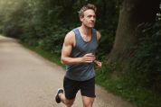 Mann joggt auf Waldweg in einem grauen Tanktop Mann joggt auf Waldweg in einem grauen Tanktop